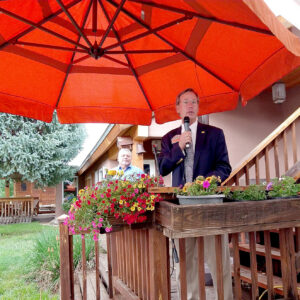 State Treasurer Tim Eichenberg under an umbrella, speaking to people in Cleveland, New Mexico, on a rainy day.